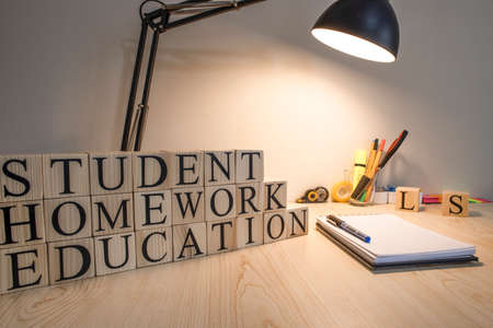 On wooden cubes, homework education student writes texts. There are desktop lamp and notepad. Consept and studio.の写真素材