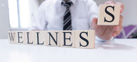 The word wellness from wooden cubes. Man in shirt and tie on the background.
