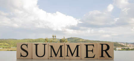 Summer text on wooden blocks. A photo was taken on the table. There are sky and mountains in the background. Conseptの写真素材