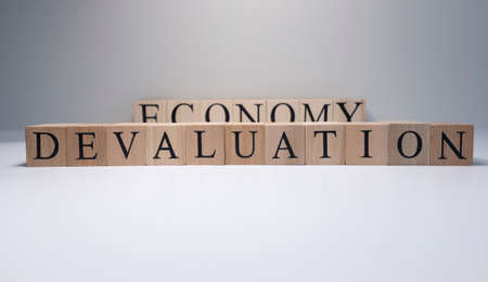 The word devaluation from wooden cubes is in the white background. Photographed in the studio and in spot light.の写真素材