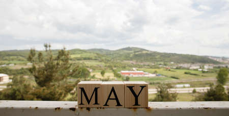 The word may from wooden cubes. Spring concept. Cloudy sky and mountains in the background.