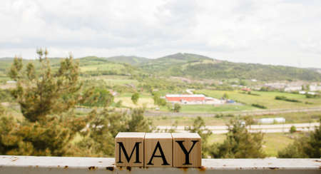 The word may from wooden cubes. Spring concept. Cloudy sky and mountains in the background.の写真素材