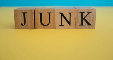 The word junk made of wooden cubes. The background is yellow and photographed in the studio.
