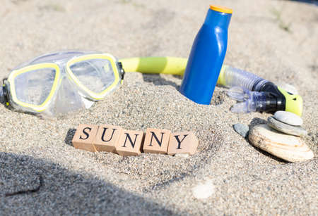 Sunny word made of wooden cubes. Sunglasses and sunscreen and slippers