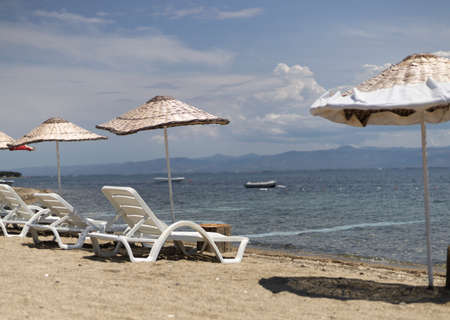 Sun beds and umbrellas by the sea. Cloudy blue sky. Photographed in the summer.の写真素材