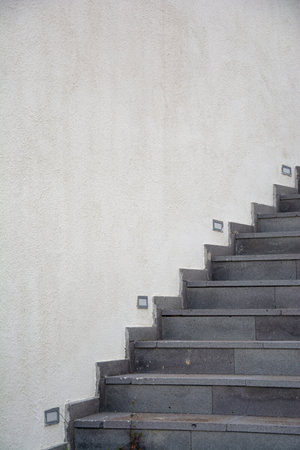 The staircase on the white wall of the building in the park, the gray stone staircase on the white cement wall background.の写真素材
