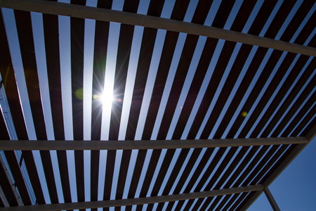 Sunlight shines through the roof of a wooden pergola on a sunny day.の写真素材