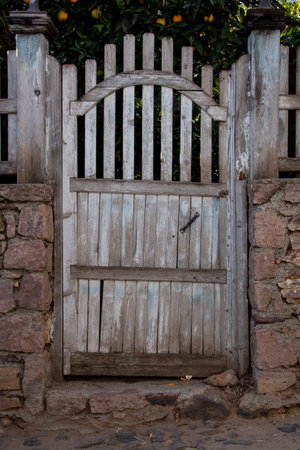 Old wooden gate in a stone wall of an old house with orange tree.の写真素材