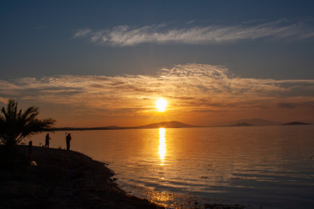 Silhouette of a man on the shore of the lake at sunset. Sunset over the sea with dramatic sky and reflection in the water.の写真素材