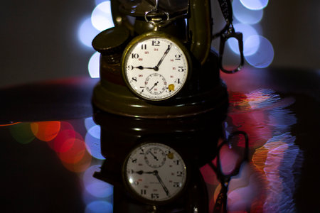 Festive decoration on bokeh background. Vintage clock on a dark background with colorful bokeh. Retro Kerosene Lamp, Classic Metal Lantern Light Decor.の写真素材
