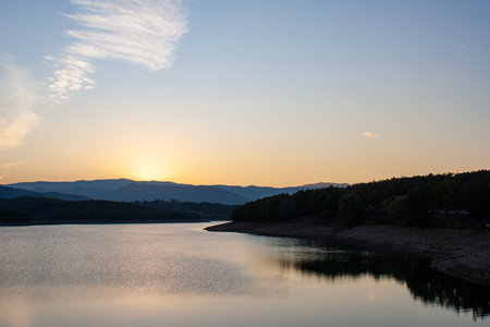 Sunset over a lake with mountains in the background and clouds in the sky. Sunset over a lake with...