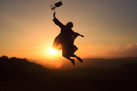 Silhouette of a young woman jumping in the air with a diploma at sunset, Concept education congratulation, Graduation Ceremony, Congratulated the graduates in University.の素材