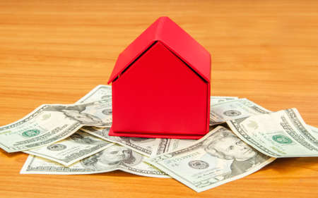 Red house on pile of money isolated on wooden backgroundの写真素材