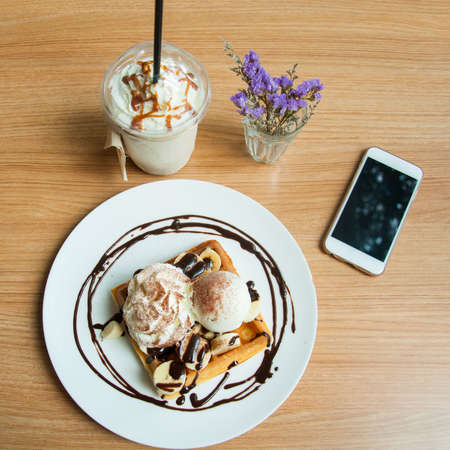 Banana ice cream ice coffee and waffle with flowers and smart phone lay on tableの写真素材