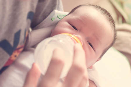 Young father feeding selective focus of newborn baby boy with milk bottle in blurred dreaming warm...