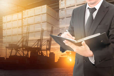 Businessman writing notebook with blurred cargo in wooden case and transportation port background, trading export abroad conceptの写真素材