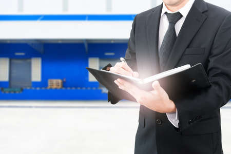 Professional businessman booking with blurred distribution warehouse background, industrial business conceptの写真素材