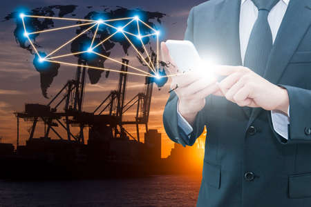 Double exposure of businessman using smart phone network connection world map , transportation port and blurred cargo warehouse background, international transportation trading business conceptの写真素材