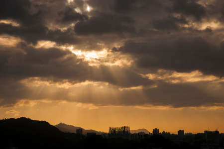 Silhouette city during warm sunset with sunray and cloudsの写真素材