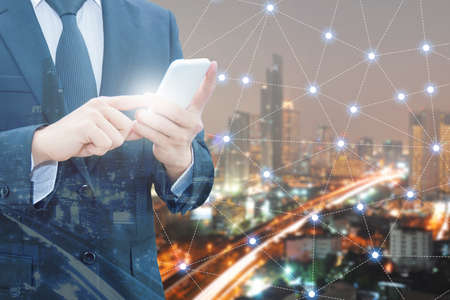 Double exposure of professional businessman using smart phone and night cityscape with network connection & blurred cityscape background, Technology , communication & Business trading conceptの写真素材