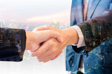 Double exposure of businessman and businesswoman handshake agree deal with city of business in blue tone backgroundの写真素材