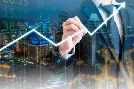 Double exposure of professional businessman with night cityscape drawing growth graph in business conceptの写真素材