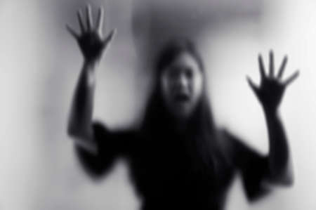 Horror scary shadow of woman behind the matte glass in black and white. Blurry hand and body figure...