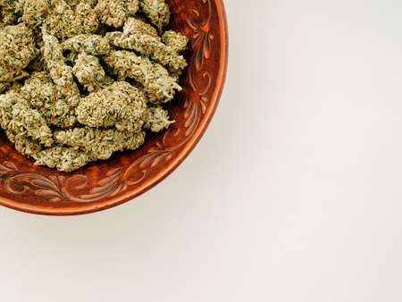 Marijuana buds in brown clay dish, flat lat, top view. Cannabis flowers and sweets on white background. Hemp recreation, pastime, legalization concept.の写真素材