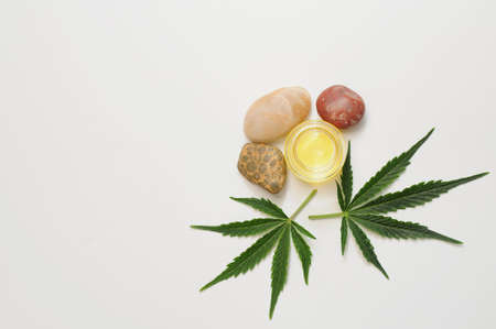 Marijuana leaves, cbd oil, sea stones, spa recreation. Fresh cannabis leaves close up, isolated on white background. Home relaxation, pastime therapy. Alternative medicine.の写真素材