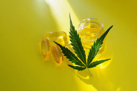 Marijuana oil, cbd recreation. Fresh cannabis leaf and medical pills on yellow background, top view, closeup. Home relaxation, pastime therapy. Alternative cosmetology.の写真素材