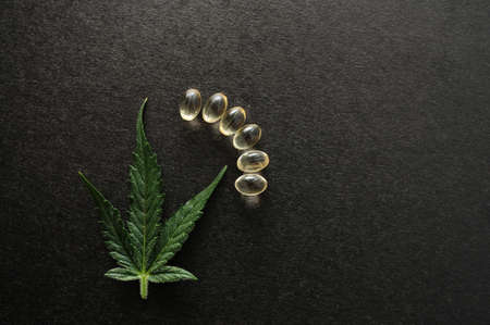 Medicinal cannabis leaves with cbd oil. Marijuana oil in medical capsules isolated on black background.の写真素材