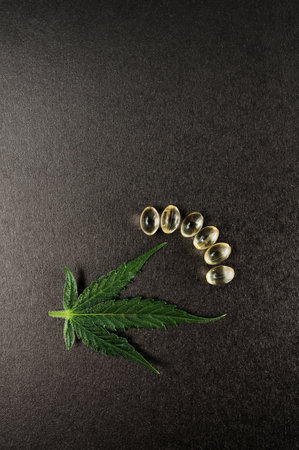 Medicinal cannabis leaves with cbd oil. Marijuana oil in medical capsules isolated on black background.の写真素材