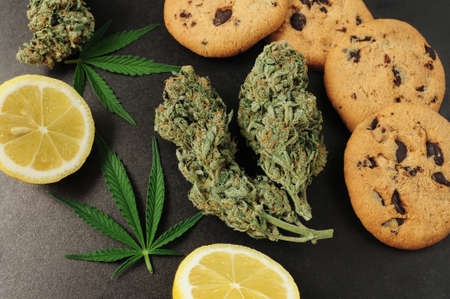 Sweets with CBD oil. Marijuana buds on black background. Cannabis flowers and chocolate cookies with nuts close-up. Top view, flat lay.の写真素材