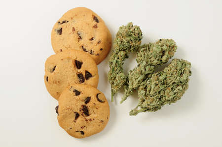 Sweets with CBD oil. Marijuana buds on white background. Cannabis flowers and chocolate cookies with nuts close-up. Top view, flat lay.の写真素材