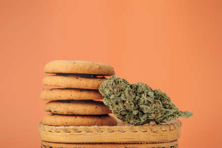 Sweets with CBD oil. Marijuana buds on orange background. Cannabis flowers and chocolate cookies with nuts close-up.の写真素材