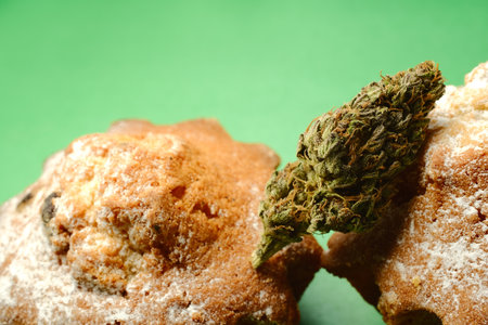 Cooked with Cannabis. Sweet cupcake with marijuana bud, macro view. Weed cakes with CBD oil and cannabis blooms isolated on green background. Marijuana Kitchen, Canna Kitchen.の写真素材