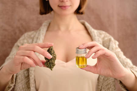 Close up of cannabis bud and cbd oil in young woman`s hands on a brown background. Medical marijuana use concept.の写真素材