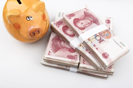 Chinese 100 RMB banknotes Stacked, with a happy piggy bank in the left top of the picture.の写真素材