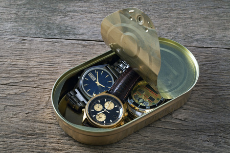 Three wristwatch in a tin on a wooden table