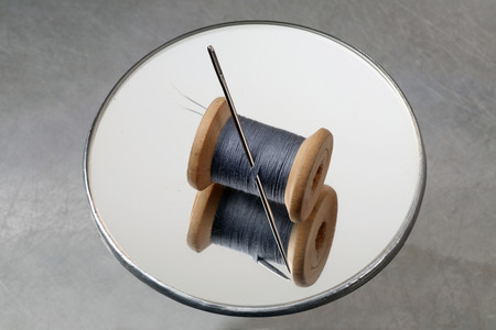 Thread reel and needle on a round mirrorの写真素材
