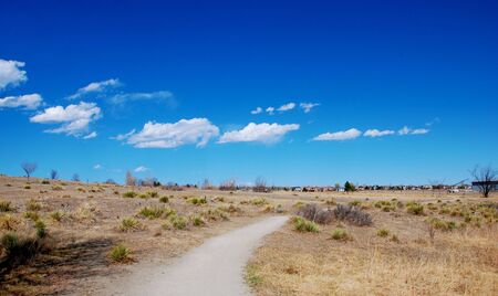 Path leads through rural prairie scenery, with a line of distant new homes on the horizon