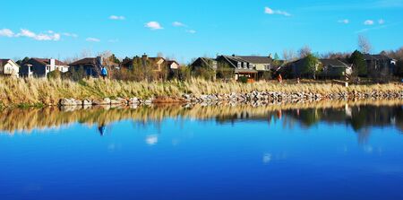 A few people walk along the weir of a peaceful suburban lakeの写真素材
