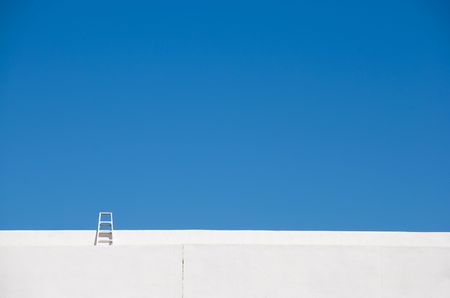 Little ladder on a bright white building reaches into a deep blue skyの写真素材