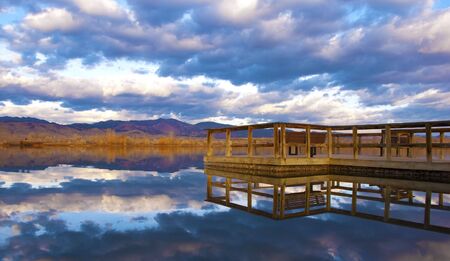 Pier with benches reaches into a small tranquil lake in the Colorado prairieの写真素材