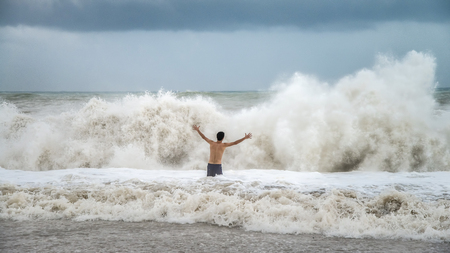 Antalya - Turkey - October 17, 2013: Young man standing against the sea waves with splash in a cloudy storm weatherの写真素材