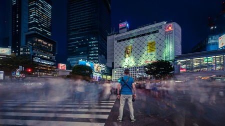 Tokyo, Japan - August 2018: Tourist with camera standing still at Shibuya Crossing with unidentified blurred pedestrians in Tokyo, Japanのeditorial素材