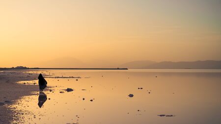 Silhouette and reflection of an unidentified Iranian woman in hijab burka near Maharloo pink lake in Shiraz, Iranの写真素材