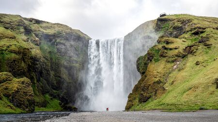 Huge waterfall of Skogafoss with a couple taking photographs in Skogar, south Icelandの写真素材
