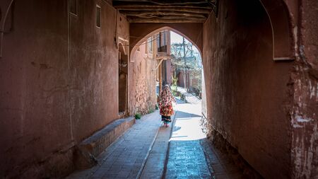 Abyaneh, Iran - May 2019: Unidentified woman with traditional Persian clothes walking down a narrow roadの写真素材