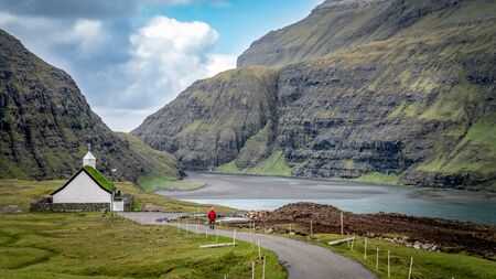 Unidentified man walking towards church from village of Saksun located on the island of Streymoy, Faroe Islands, Denmarkの写真素材